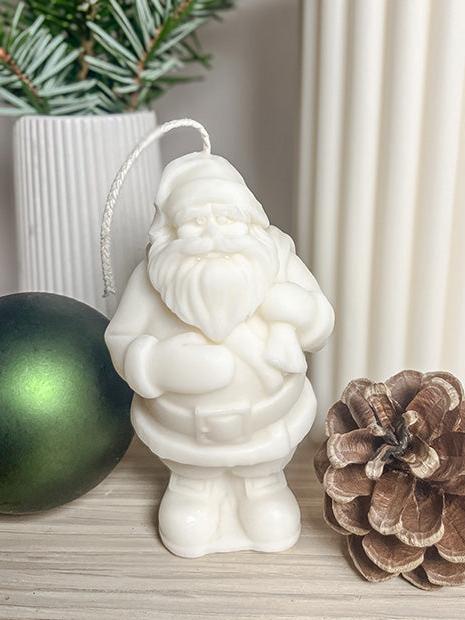 Julemand sojalys omgivet af gran, kogle, grøn kugle og et tændt lys bagved – dekorativ og bæredygtig julepynt.