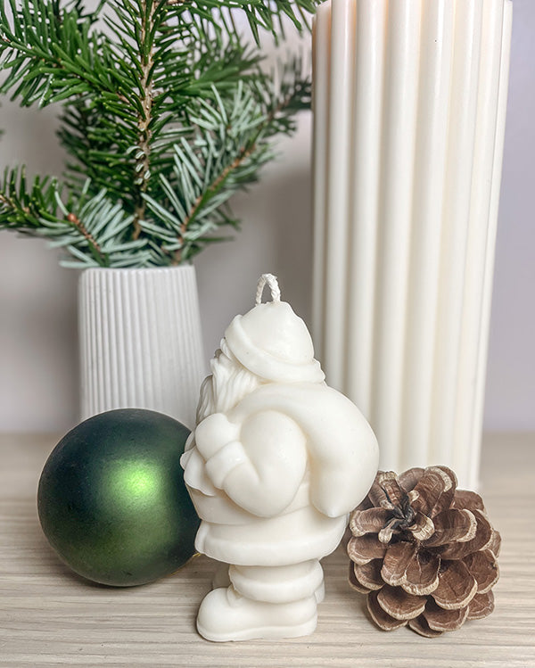 Håndlavet julemand sojalys set fra siden, med gran, kogle og grøn julepynt omkring.