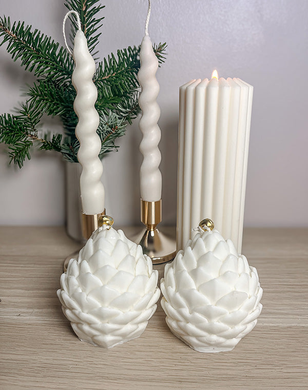 To kogle sojalys foran et smukt julearrangement med vase med gran, snoede stagelys og bloklys – elegant og stemningsfuld dekoration.