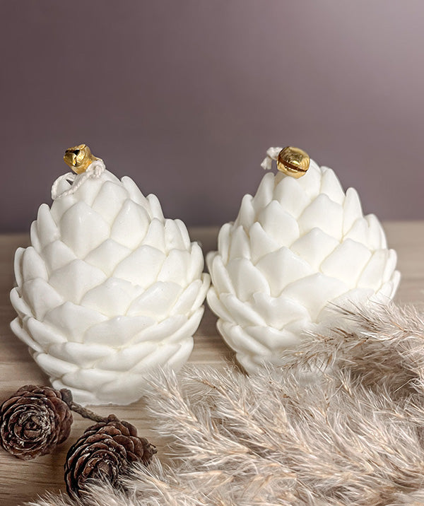 To elegante kogle sojalys dekoreret med naturlige elementer som kogle og pampasgræs – hyggelig og rolig vinterstemning.