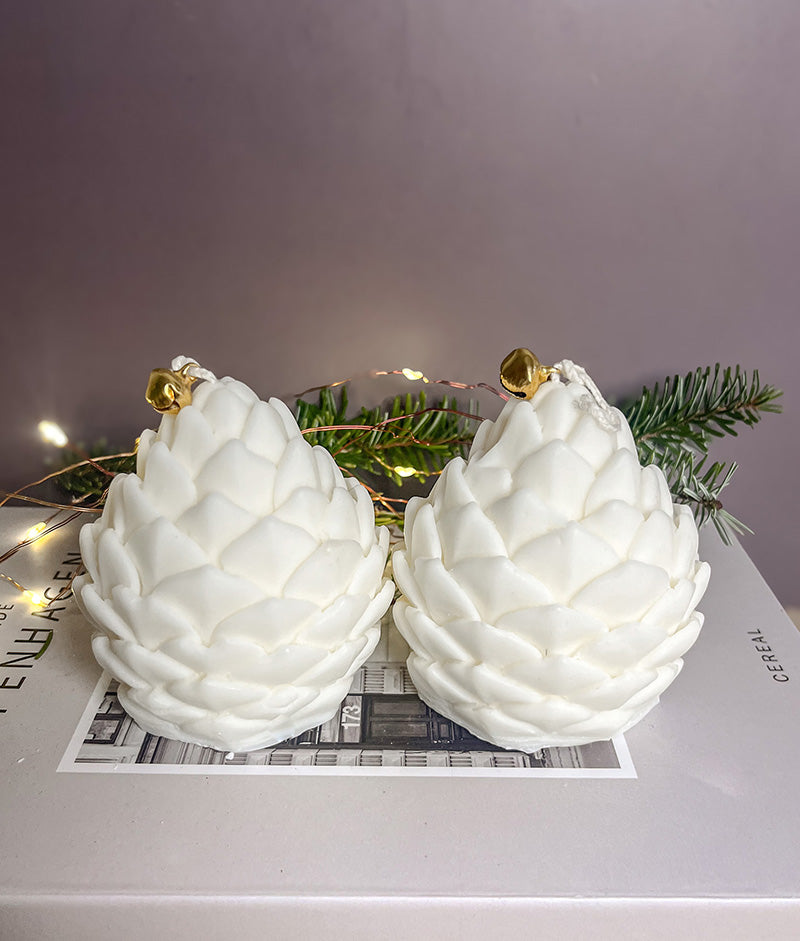 To håndlavede kogle sojalys på en bog med gran og lyskæde bagved – hyggelig og stemningsfuld juledekoration.