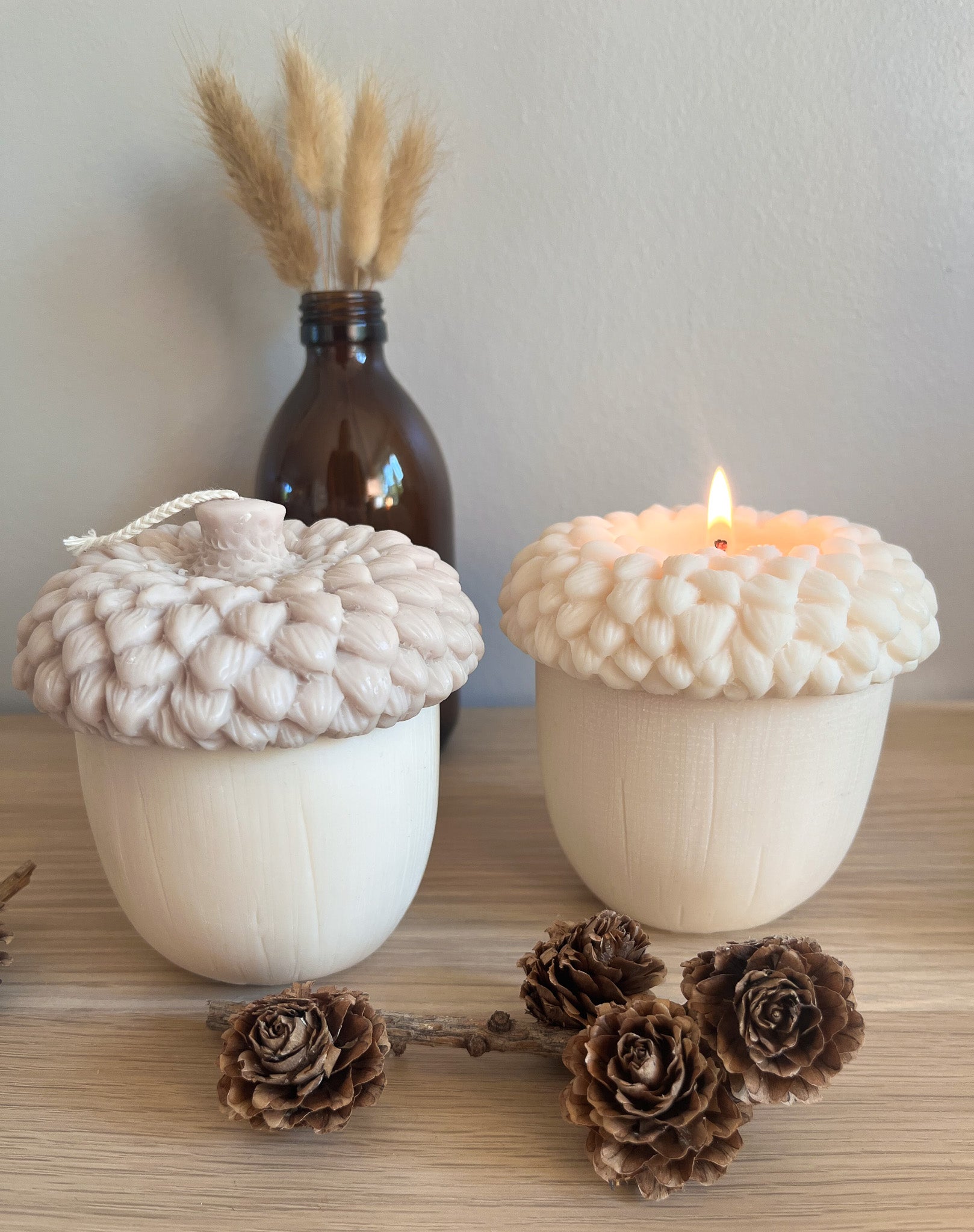 To ahorn sojalys, et beige og et hvidt, pyntet med grankogler og vase i baggrunden. Skaber naturlig efterårsstemning.