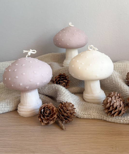 Tre svampe sojalys, to beige og et hvidt, dekoreret med kogler. Skaber en varm og organisk stemning.