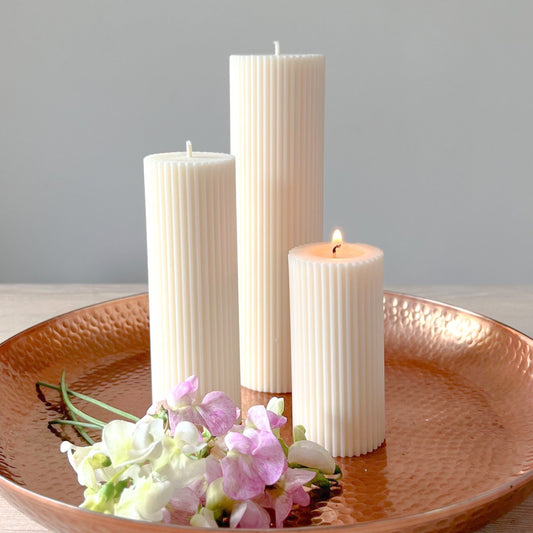Minimalistiske bloklys med dine lodrette linjer på et messing fad og blomster